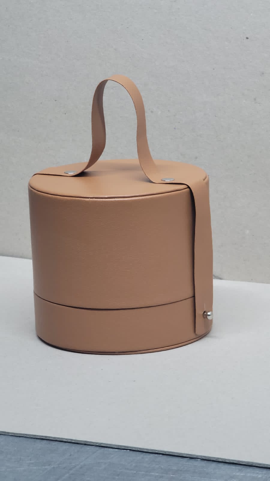 Coffret artisanal en simili cuir rond, couleur camel, avec une anse pour une manipulation facile, symbolisant l'artisanat de qualité.