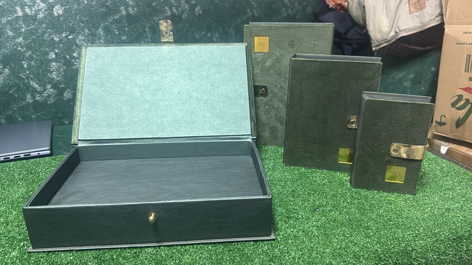 Pile de boîtes rigides en velours vert, style vintage, avec plaque dorée.