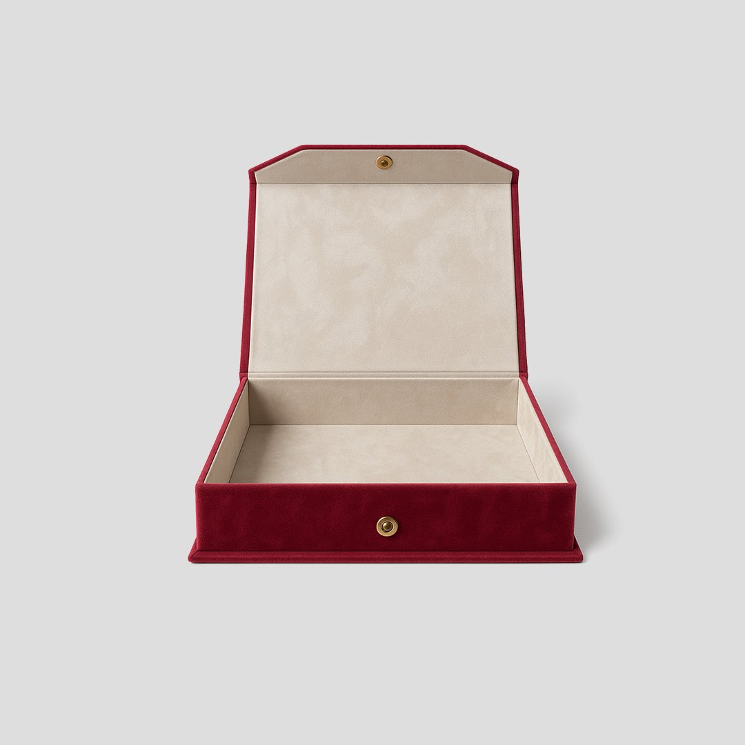 Coffret vide en velours rouge avec intérieur doublé velours, posé sur fond vert.